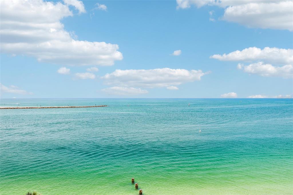 A balcony with tiled flooring and a glass railing overlooks the ocean and a pool — 450 S GULFVIEW BOULEVARD UNIT 703, CLEARWATER, FL