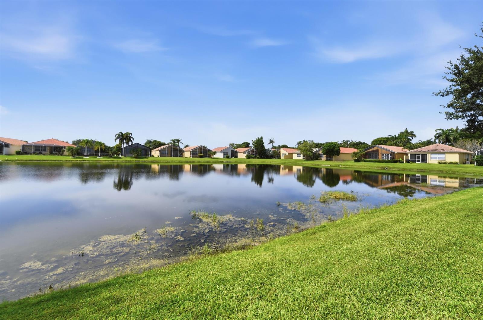 A row of suburban houses sits behind a calm lake with a grassy foreground — 7229 Cataluna Circle, Delray Beach FL 33446, DELRAY BEACH, FL