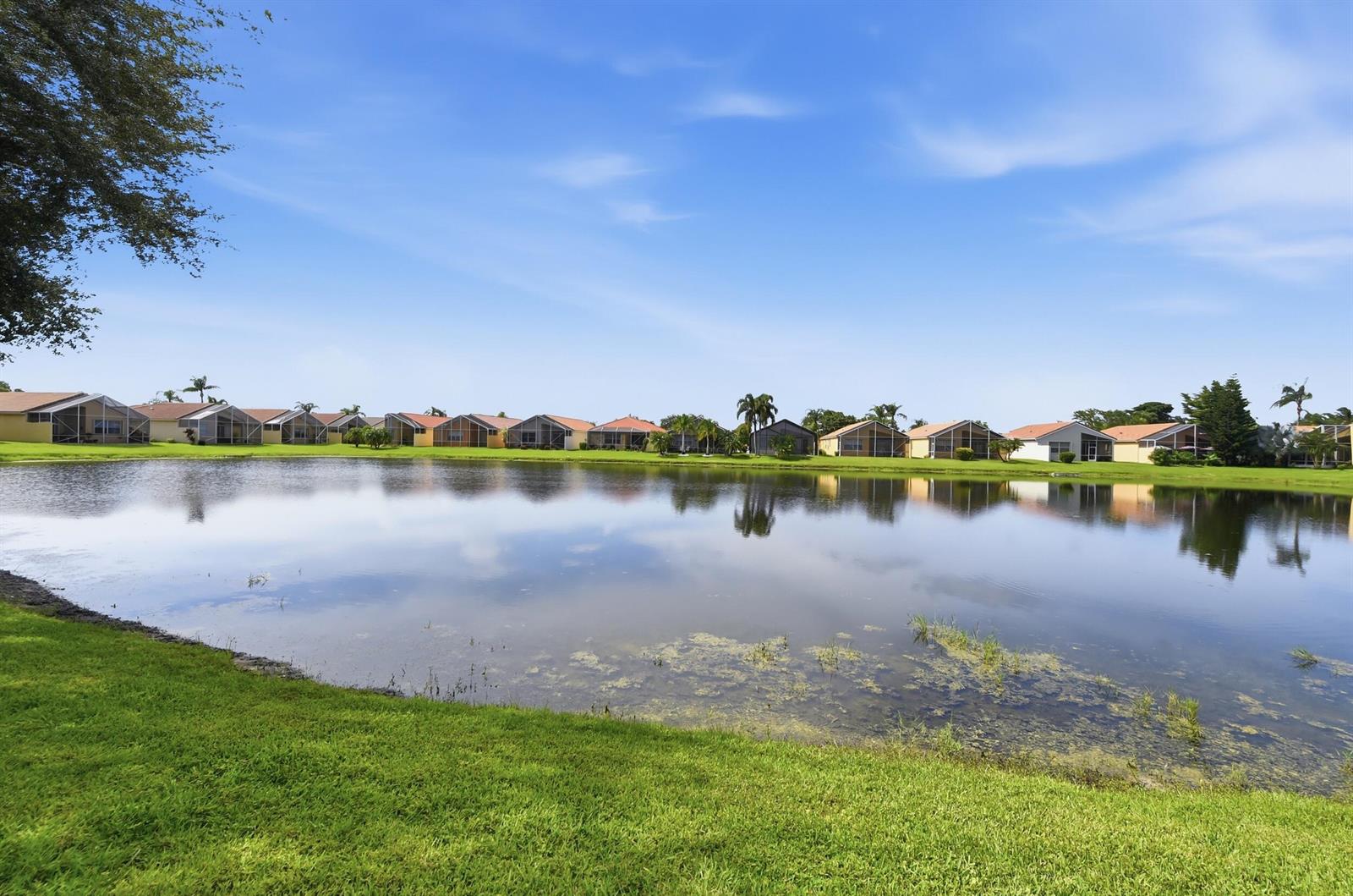 A row of suburban houses sits across a pond with a grassy foreground — 7229 Cataluna Circle, Delray Beach FL 33446, DELRAY BEACH, FL