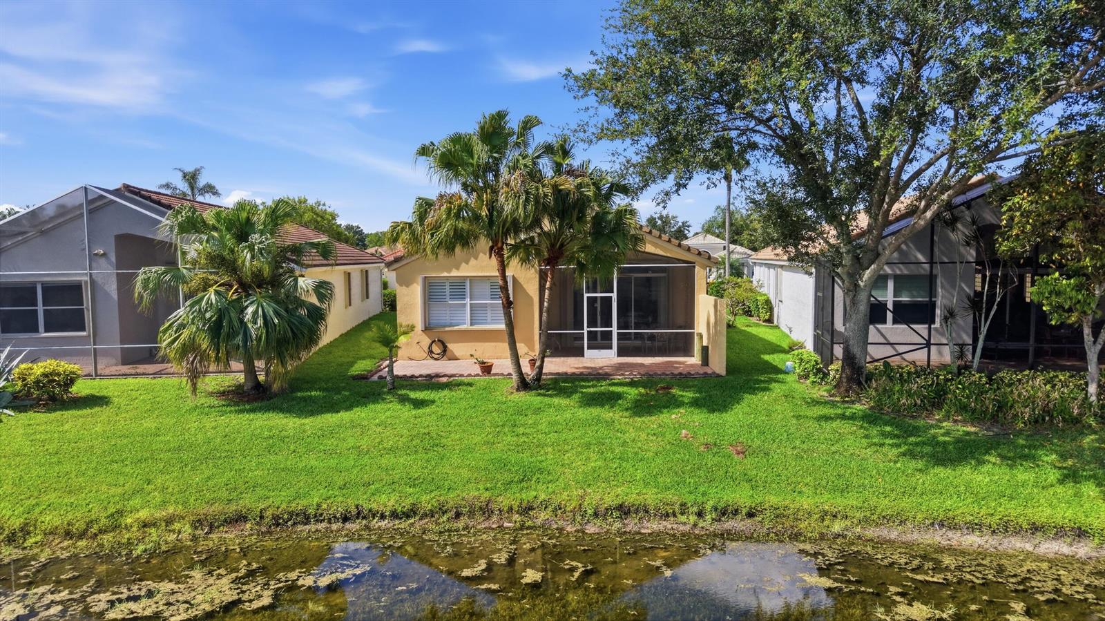 A yellow house with a screened-in patio sits behind a lawn and a small pond — 7229 Cataluna Circle, Delray Beach FL 33446, DELRAY BEACH, FL