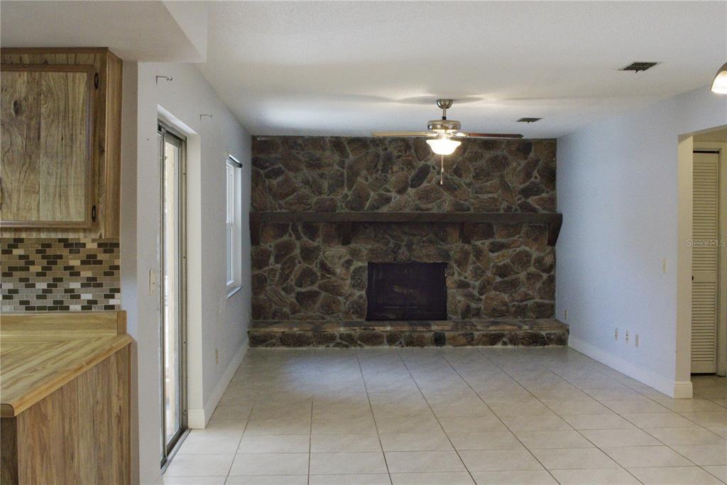 A living room features a large stone fireplace, tile flooring, and a ceiling fan — 3740 HAWTHORNE LANE, WINTER PARK, FL