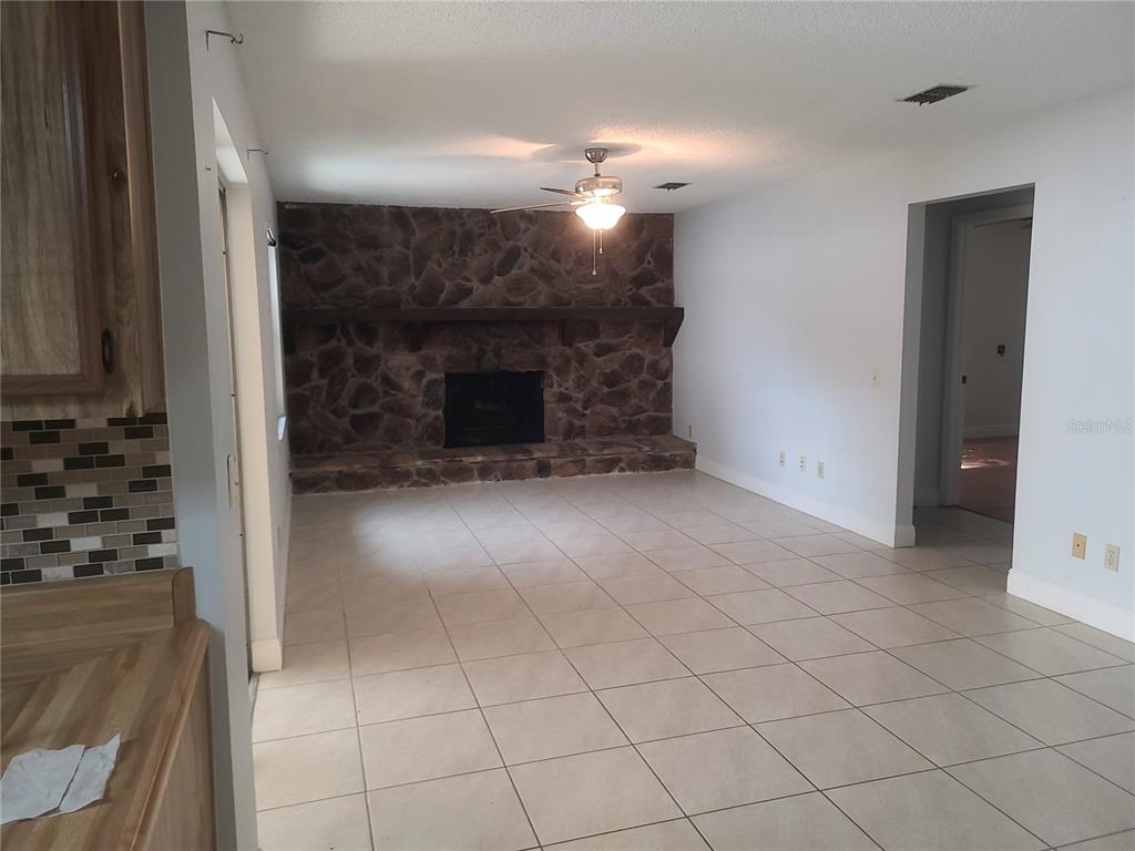 A living room features a stone fireplace, a ceiling fan, and light-colored tile flooring — 3740 HAWTHORNE LANE, WINTER PARK, FL