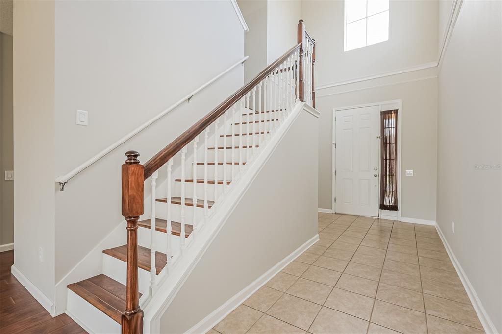 A foyer features a staircase with wooden treads and white railings next to a front door — 13955 CRATER CIRCLE, HUDSON, FL