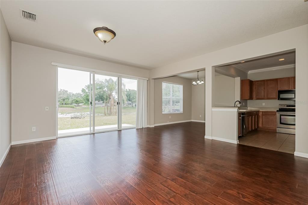 A living room with dark wood floors, a sliding glass door, and an adjacent kitchen — 13955 CRATER CIRCLE, HUDSON, FL