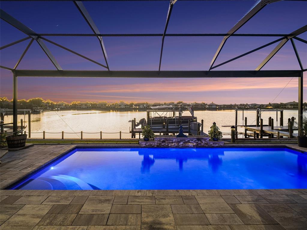A swimming pool sits on a patio under a screened enclosure overlooking a lake — 1018 OVERLOOK COURT, BRADENTON, FL