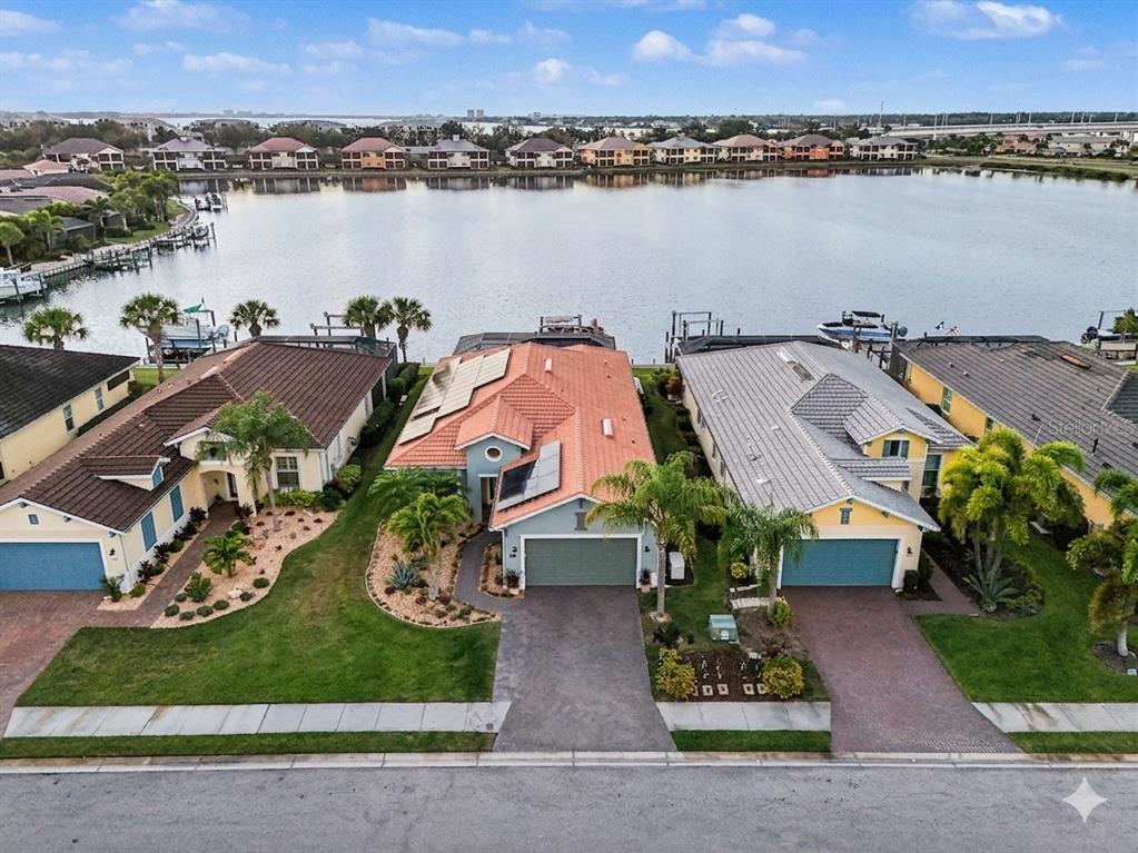 An aerial view shows three waterfront houses with tiled roofs and attached garages along a lake — 1018 OVERLOOK COURT, BRADENTON, FL