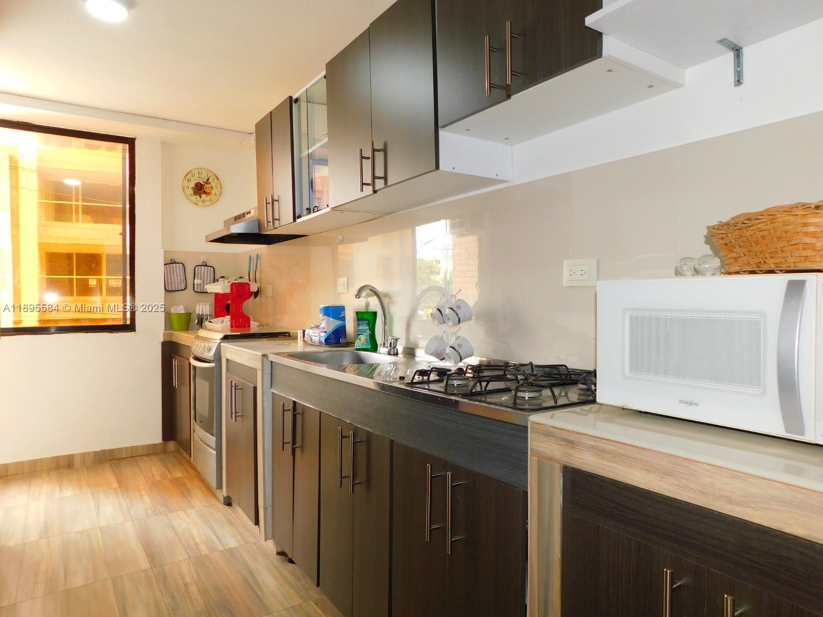 A kitchen features dark wood cabinets, a stainless steel sink, a gas stove, and tile flooring — 77-53 57 Ave # 2, xx, xx