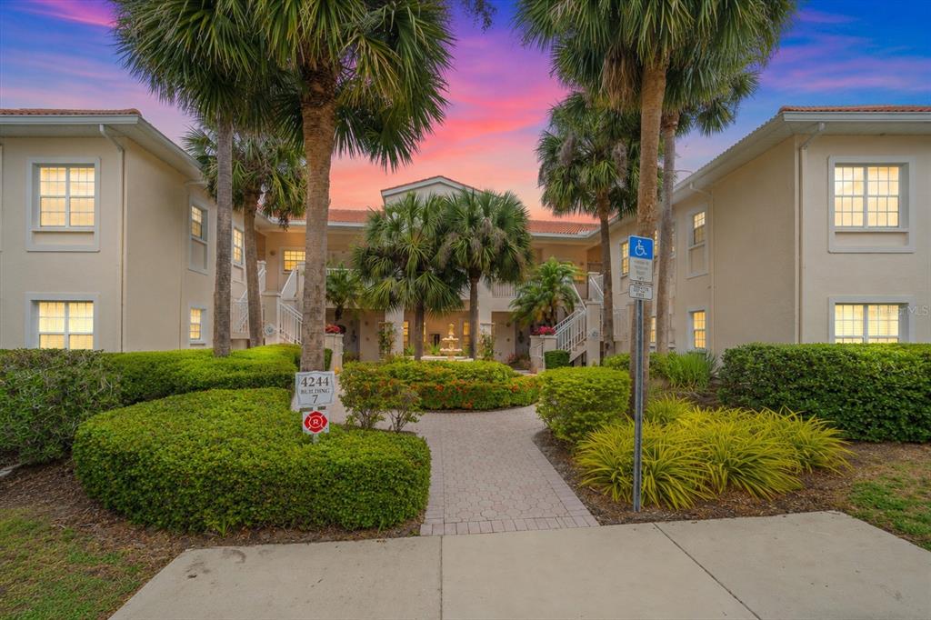 A paved walkway leads to the entrance of a two-story apartment building with landscaping — 4244 CENTRAL SARASOTA PARKWAY UNIT 714, SARASOTA, FL