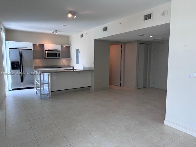 A modern kitchen with white cabinetry and stainless steel appliances opens to a tiled living area — 185 SW 7th St # 2300, Miami FL 33130, MIAMI, FL