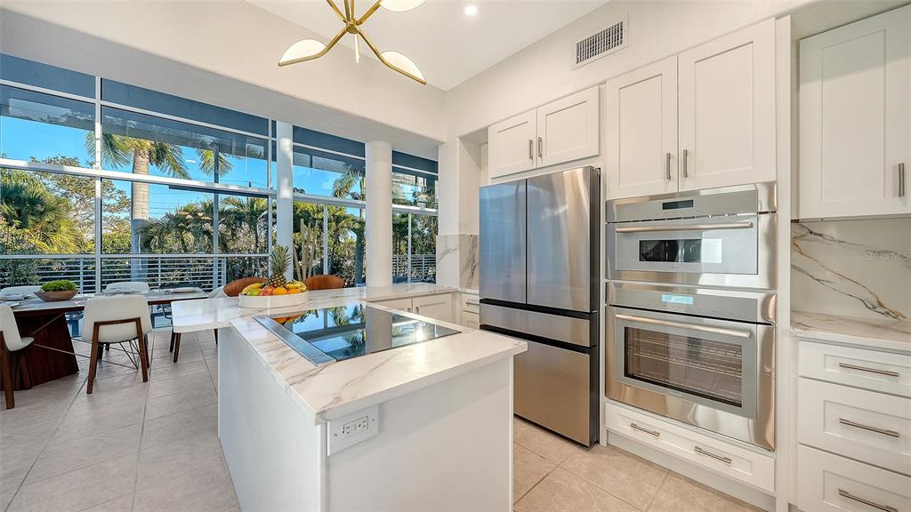 A modern kitchen features a marble-topped island, stainless steel appliances, and large floor-to-ceiling windows — 1168 WESTWAY DRIVE, SARASOTA, FL