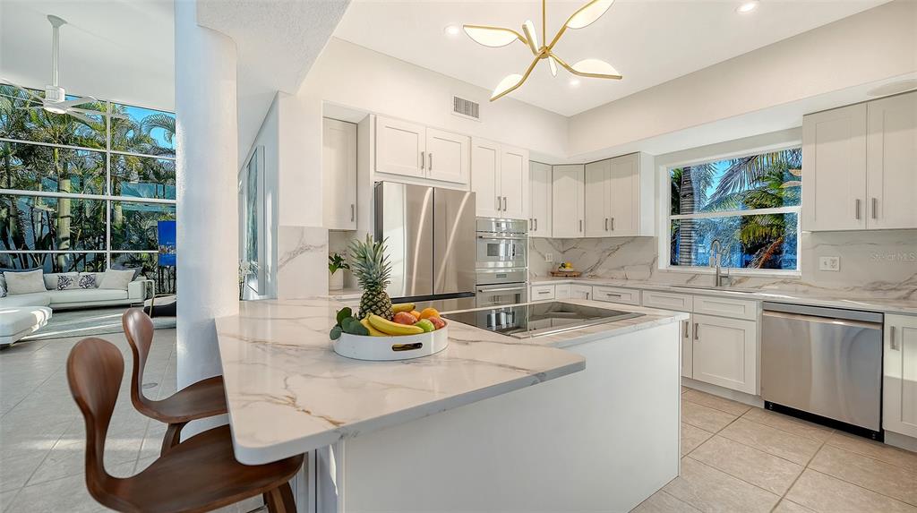 A modern kitchen features white cabinetry, marble-look countertops, stainless steel appliances, and a breakfast bar — 1168 WESTWAY DRIVE, SARASOTA, FL