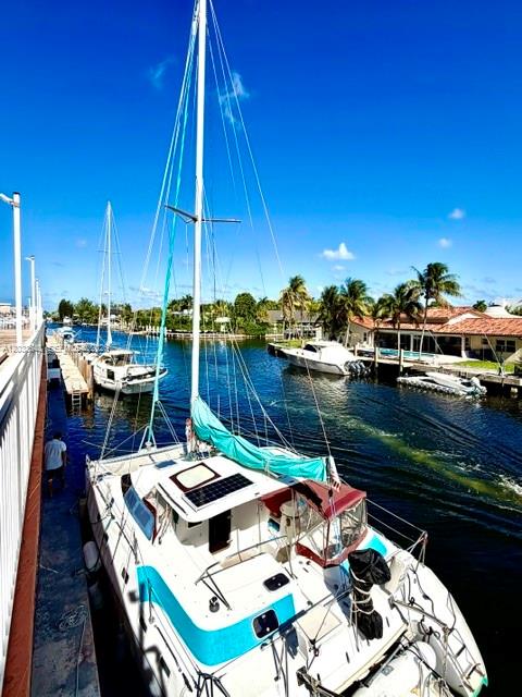 A sailboat is docked at a canal-side pier near waterfront homes and palm trees — 2450 NE 135th St # 704, North Miami FL 33181, NORTH MIAMI, FL