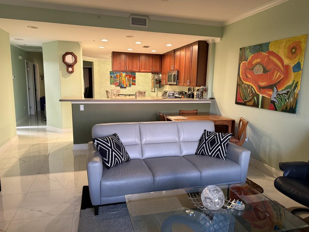 A living room with a gray sofa, glass coffee table, and an open kitchen area — 7194 KEY HAVEN ROAD UNIT 504, SEMINOLE, FL