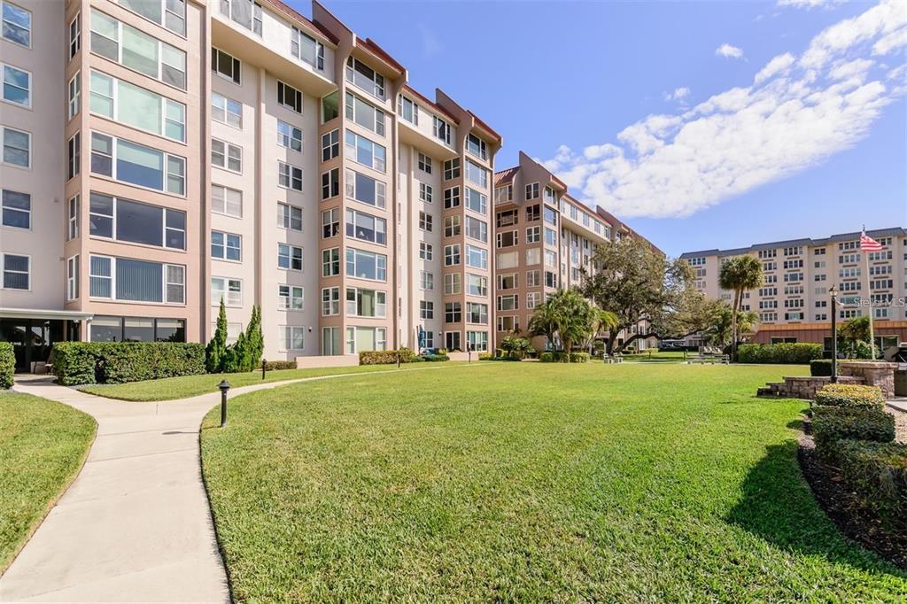 A multi-story apartment building overlooks a large green lawn with a paved walkway — 632 EDGEWATER DRIVE UNIT 139, DUNEDIN, FL