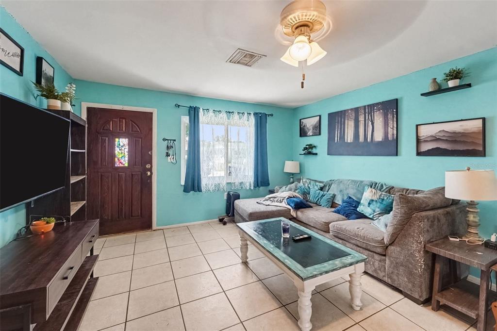 A living room with turquoise walls, a grey sectional sofa, tiled floors, and a ceiling fan — 8143 HIXTON DRIVE, PORT RICHEY, FL