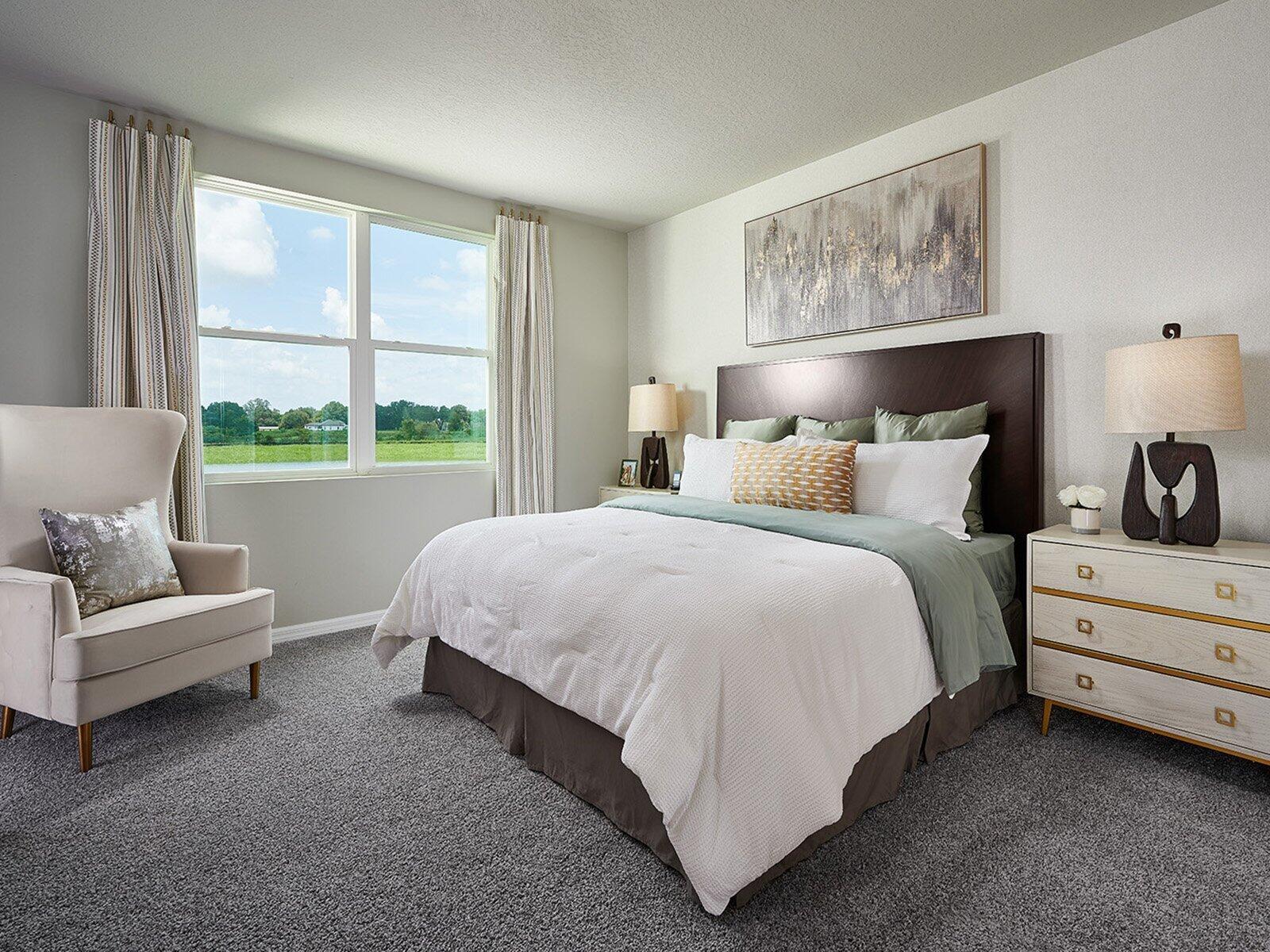 A bedroom features a queen bed, a beige armchair, and a window overlooking a grassy field — 5457 Hampton Park Circle, Vero Beach FL 32966, VERO BEACH, FL