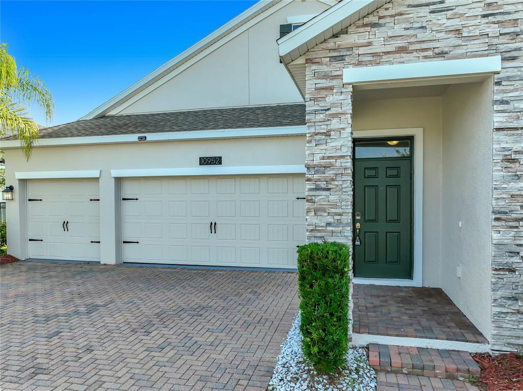 A beige house exterior features a two-car garage, a stone-accented entryway, and a green door — 10952 LONGLEAF WOODS DRIVE, ORLANDO, FL