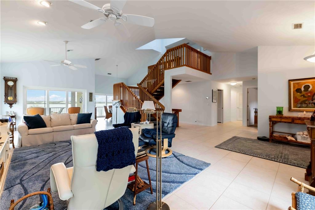 A spacious living room features a wooden staircase, tiled floors, and a blue area rug — 7795 MANASOTA KEY ROAD, ENGLEWOOD, FL