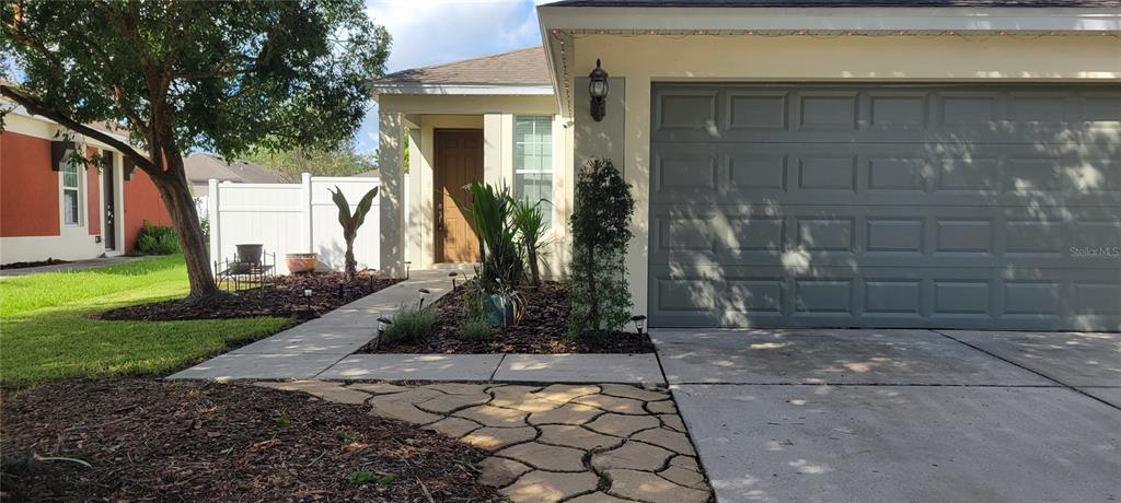 The exterior of a house features a gray garage door, a front door, and landscaping — 1109 CHINA ASTER WAY, BROOKSVILLE, FL