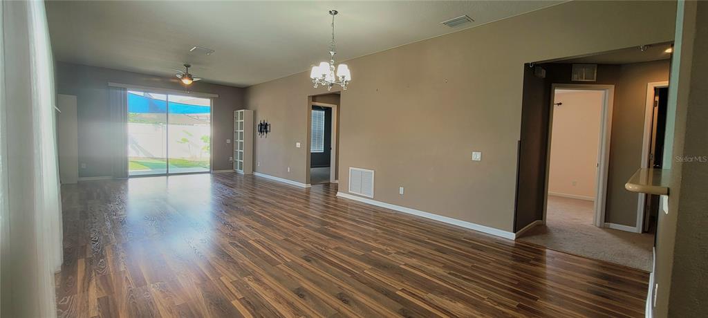 A spacious living room features wood-look flooring, a chandelier, and sliding glass doors to outside — 1109 CHINA ASTER WAY, BROOKSVILLE, FL