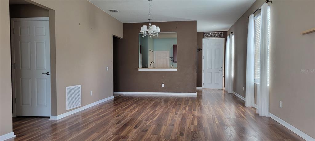 A living room with wood-look flooring, a chandelier, and a pass-through window to the kitchen — 1109 CHINA ASTER WAY, BROOKSVILLE, FL