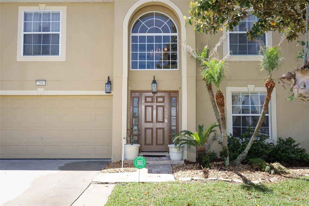 A two-story house exterior features a beige stucco facade, a garage, and a front entrance — 210 PINEFIELD DRIVE, SANFORD, FL
