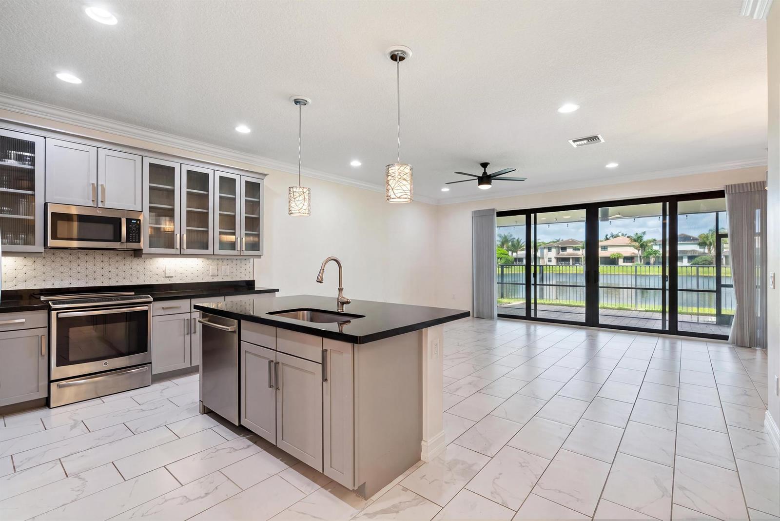A modern kitchen features gray cabinets, black countertops, and tile flooring overlooking a lake view — 13809 Imperial Topaz Trail, Delray Beach FL 33446, DELRAY BEACH, FL