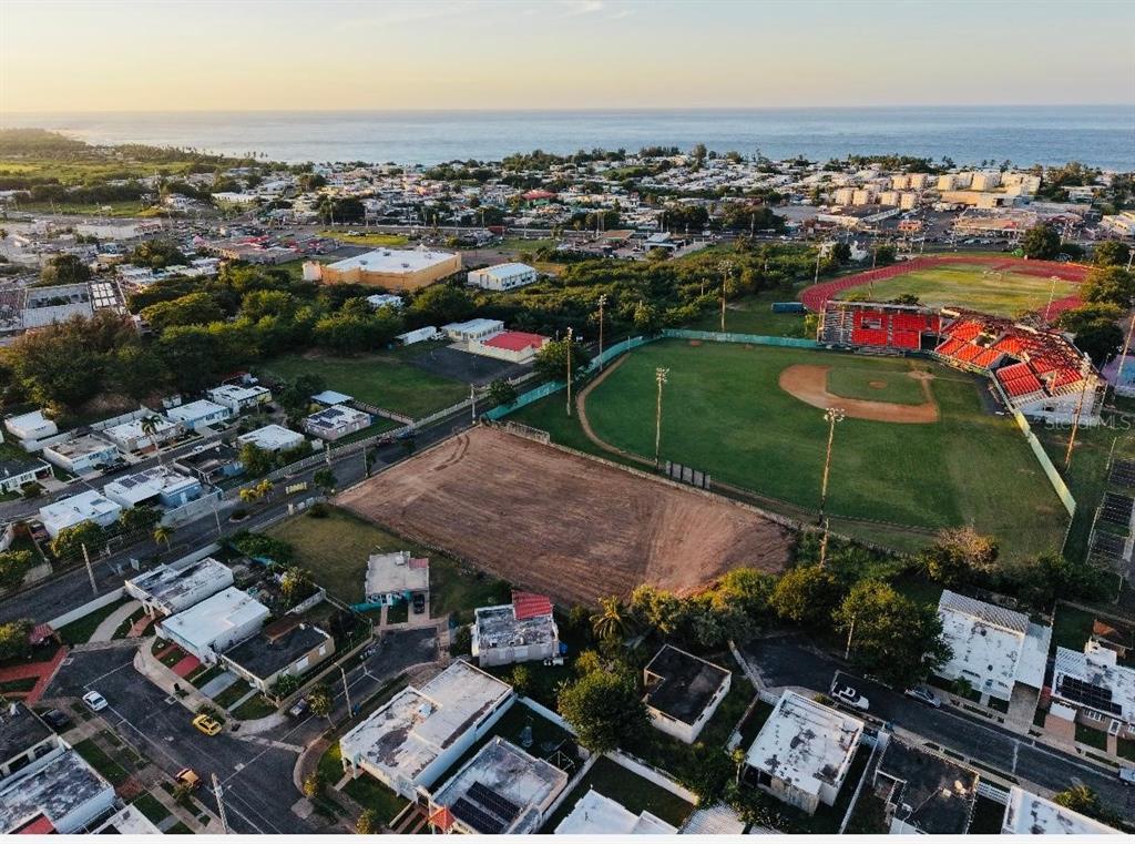 An aerial view shows a baseball field, a dirt lot, and surrounding residential houses near water — N BO. PUEBLO, HATILLO, PR