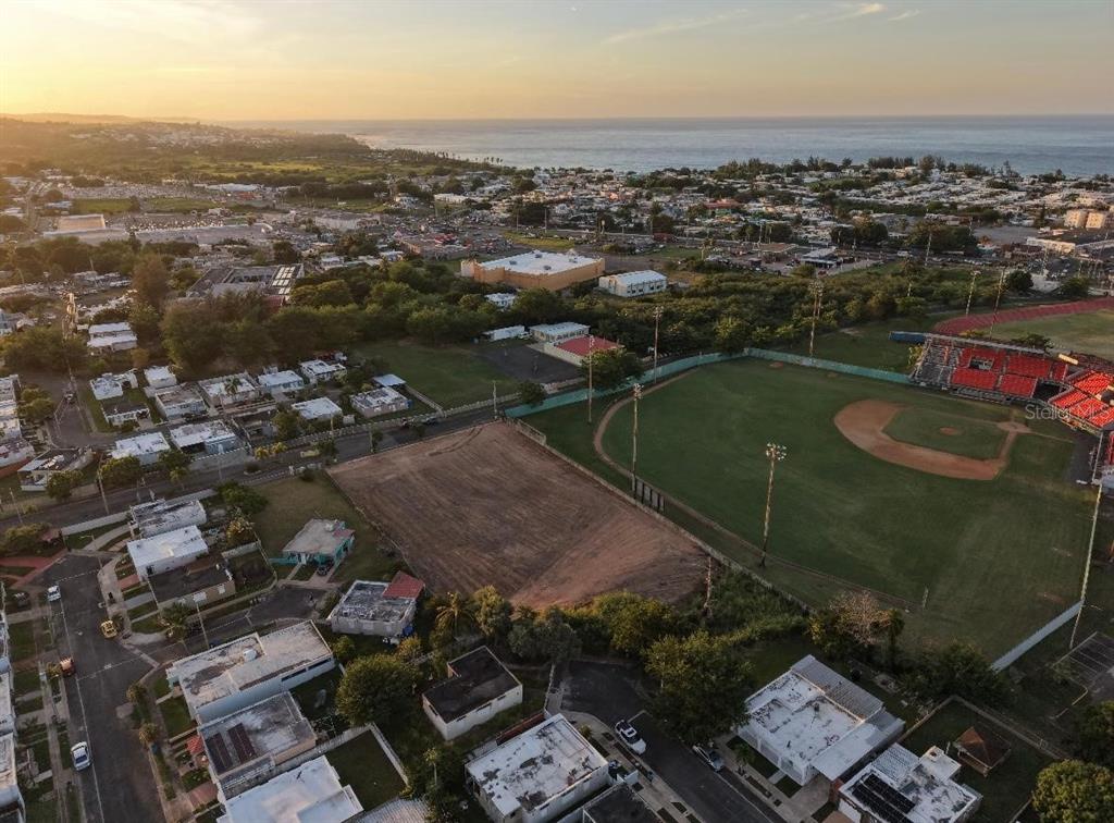 Aerial view of a baseball field, a vacant lot, and surrounding residential neighborhood near the ocean — N BO. PUEBLO, HATILLO, PR