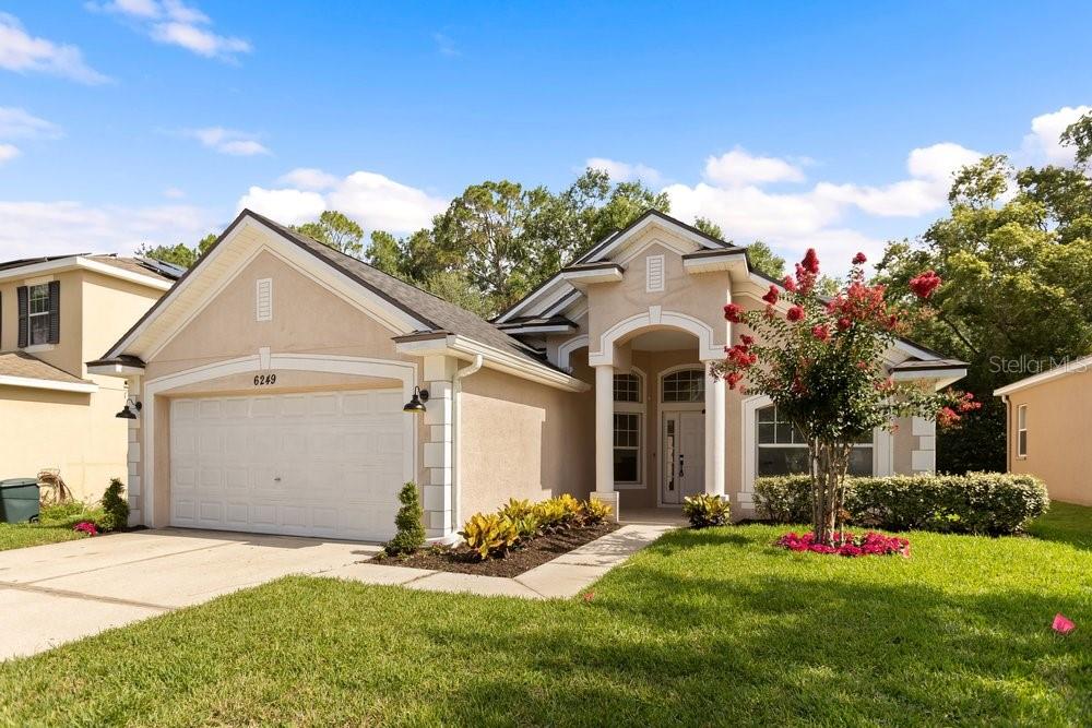 A single-story suburban house with a beige stucco exterior, a two-car garage, and landscaping — 6249 TWIN BRIDGES DRIVE, ZEPHYRHILLS, FL