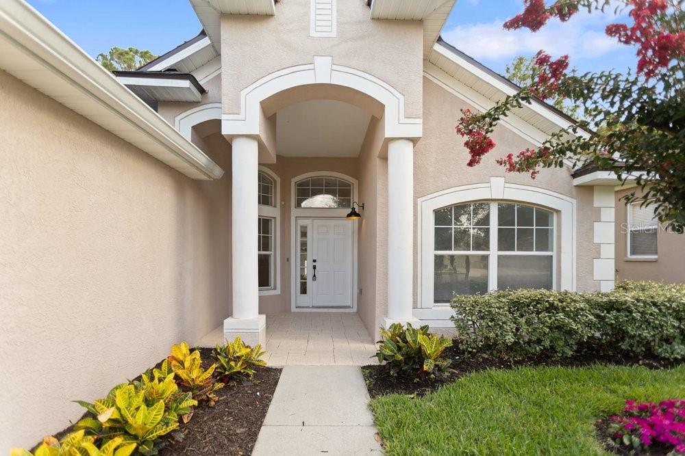 The exterior of a house features a covered entryway with two white columns and landscaping — 6249 TWIN BRIDGES DRIVE, ZEPHYRHILLS, FL