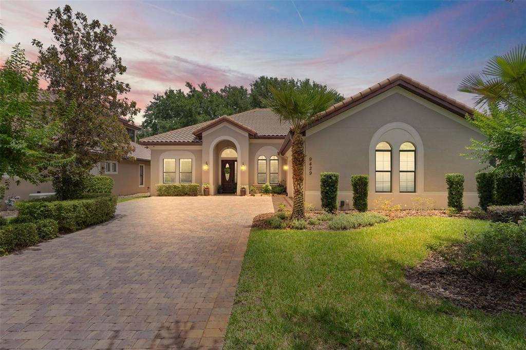 A single-story house with a paved driveway, arched entryway, and a tiled roof at sunset — 9429 SAN MIGUEL, HOWEY IN THE HILLS, FL
