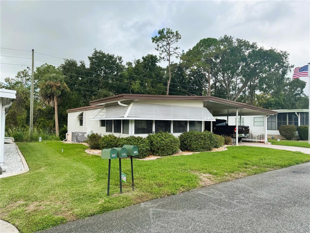 A single-story mobile home with a carport, white siding, and green mailboxes in the yard — 131 BOUGAINVILLEA DRIVE, LEESBURG, FL