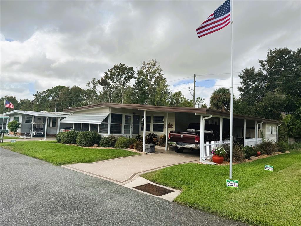 A single-story manufactured home with a carport, a driveway, and an American flag — 131 BOUGAINVILLEA DRIVE, LEESBURG, FL