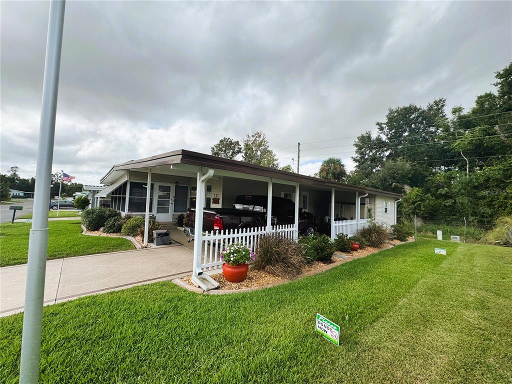 A single-story manufactured home features a covered carport, white picket fence, and landscaped lawn — 131 BOUGAINVILLEA DRIVE, LEESBURG, FL