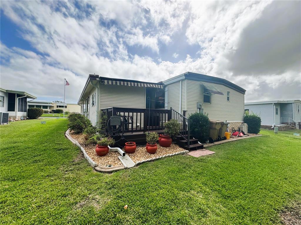A mobile home exterior featuring a wooden deck, gravel landscaping, and potted plants — 131 BOUGAINVILLEA DRIVE, LEESBURG, FL