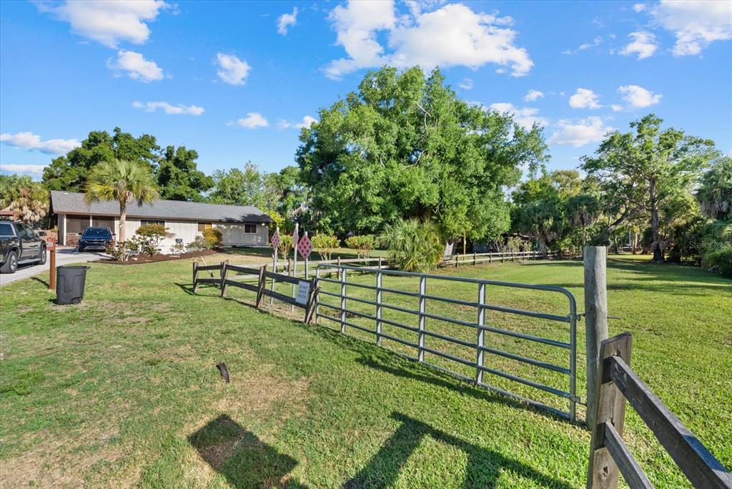 A metal gate and wooden fence enclose a grassy yard in front of a house — Lot 8 & 9 NUTMEG AVENUE, SARASOTA, FL