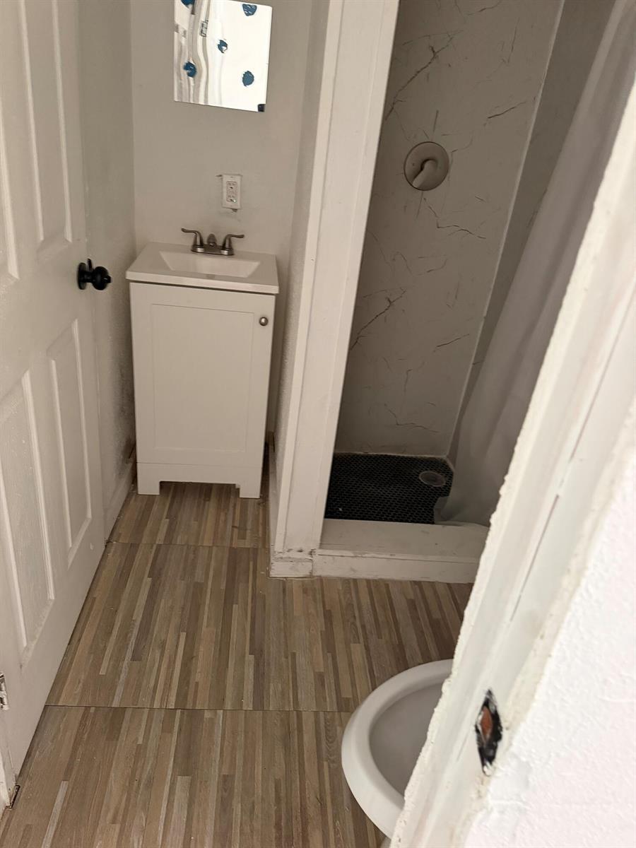 A small bathroom features a white vanity, a walk-in shower, and wood-look tile flooring — 8556 BERKLEY Drive, Davie FL 33324, DAVIE, FL