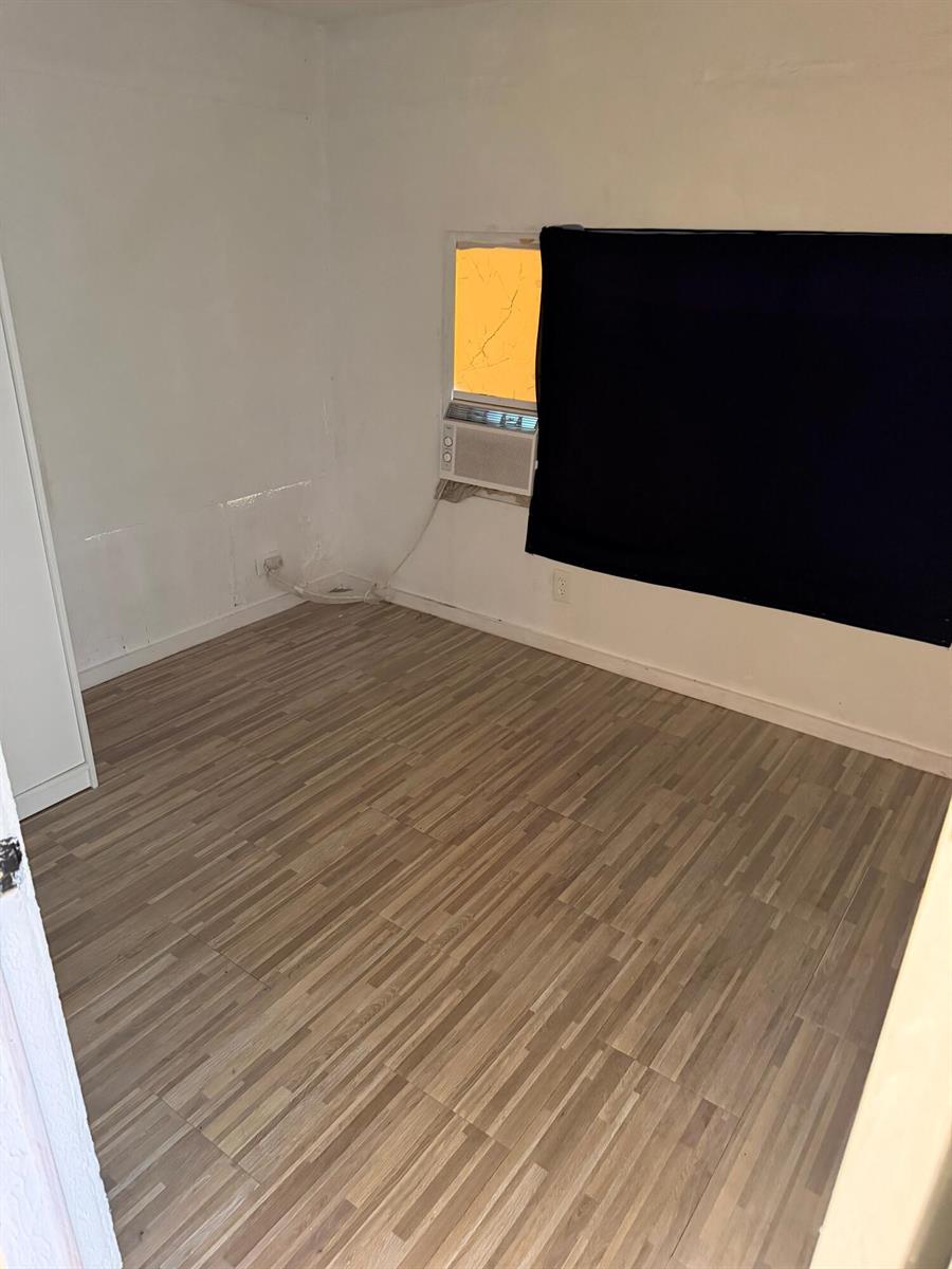 An empty room with wood-look flooring, white walls, and a window air conditioning unit — 8556 BERKLEY Drive, Davie FL 33324, DAVIE, FL