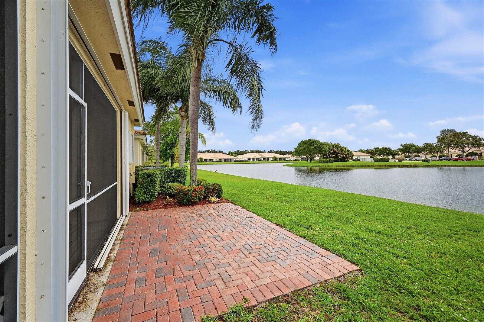 A brick patio sits beside a screened-in porch overlooking a lake and grassy lawn — 2340 Windjammer Way, West Palm Beach FL 33411, WEST PALM BEACH, FL