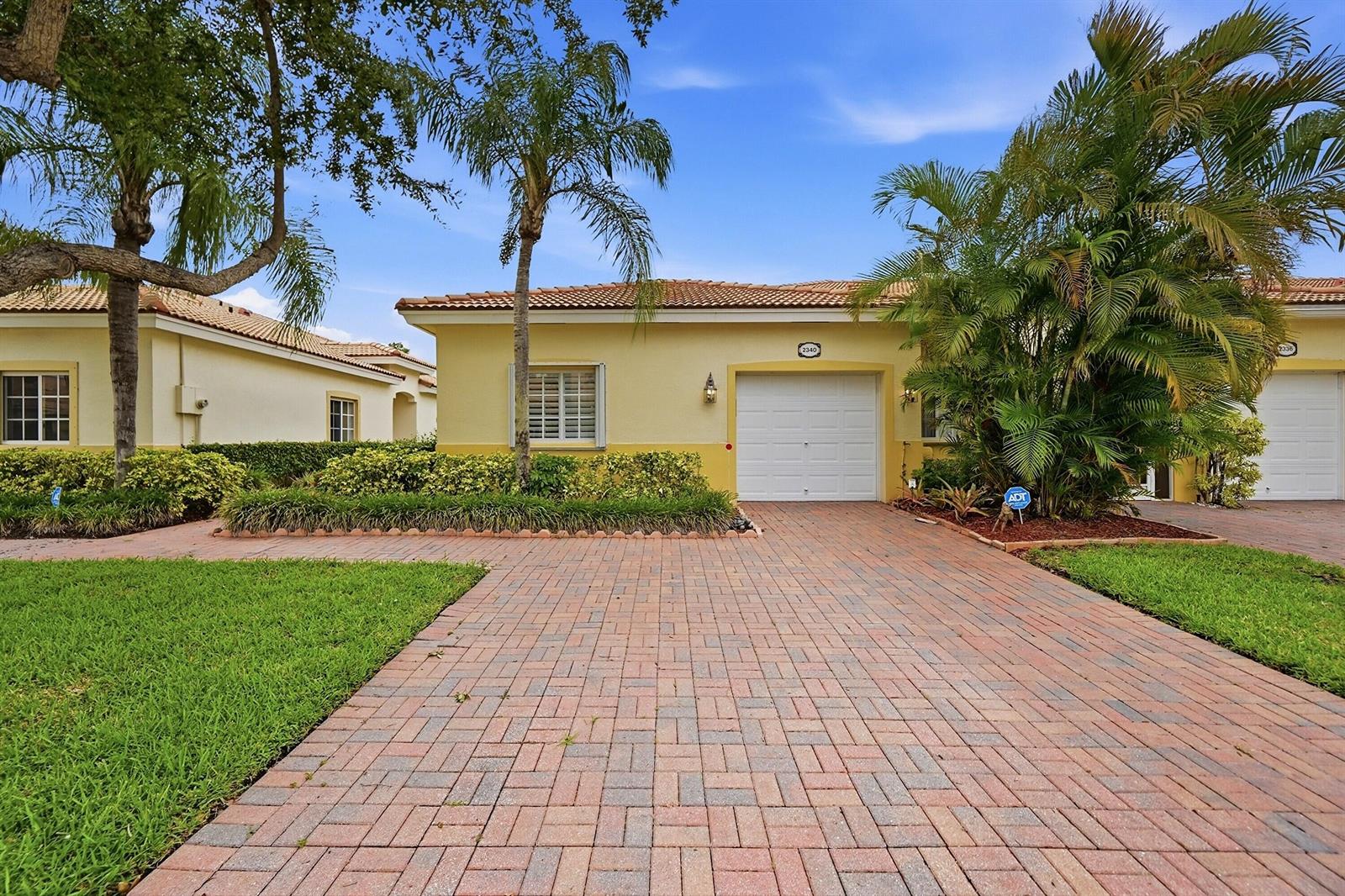 A yellow single-story house with a brick paver driveway and a white garage door — 2340 Windjammer Way, West Palm Beach FL 33411, WEST PALM BEACH, FL