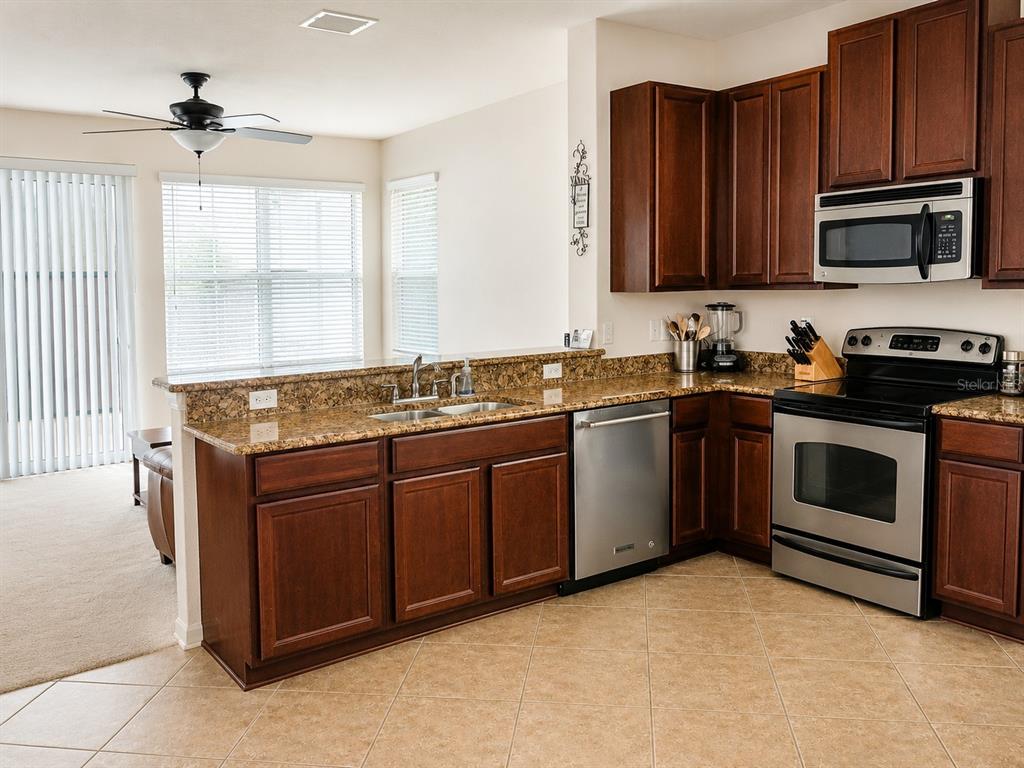 A kitchen features dark wood cabinets, granite countertops, stainless steel appliances, and tile flooring — 10311 GREYSTONE RIDGE COURT, RIVERVIEW, FL