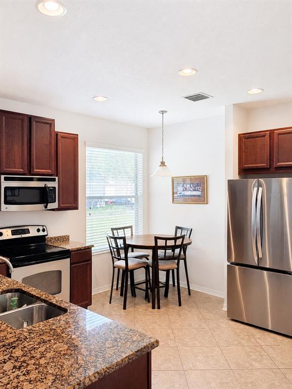 A kitchen features dark wood cabinets, granite countertops, stainless steel appliances, and a dining area — 10311 GREYSTONE RIDGE COURT, RIVERVIEW, FL