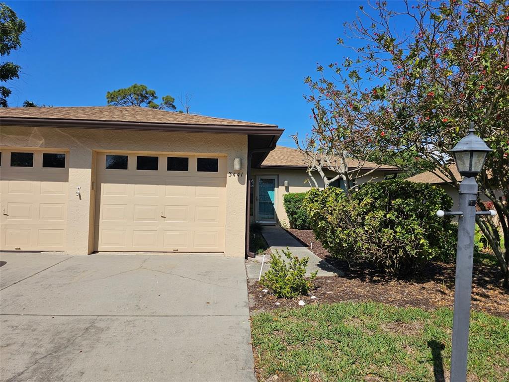 A tan single-story house exterior features a two-car garage and a front walkway — 3441 51ST AVENUE CIRCLE W UNIT 213, BRADENTON, FL