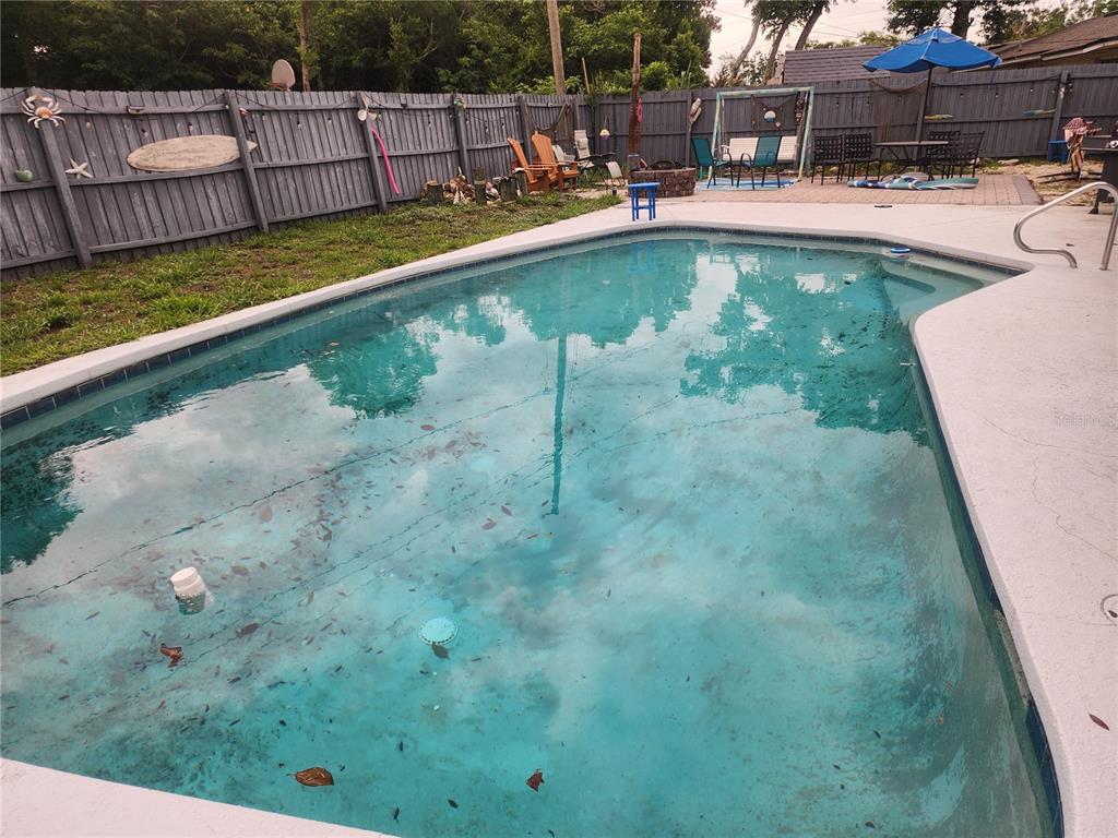 A backyard swimming pool with debris on the bottom sits next to a wooden fence — 2054 EASTBROOK BOULEVARD, WINTER PARK, FL