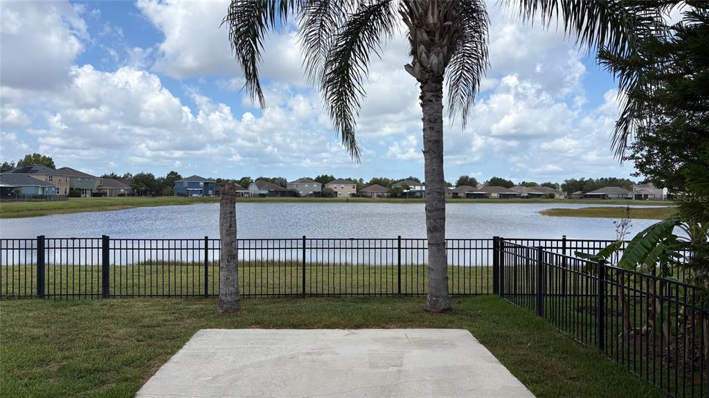 A concrete patio overlooks a fenced backyard, a pond, and several houses under a cloudy sky — 10152 CELTIC ASH DRIVE, RUSKIN, FL