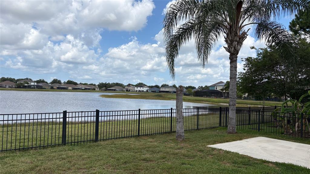 A fenced backyard overlooks a large pond with houses visible in the distance — 10152 CELTIC ASH DRIVE, RUSKIN, FL