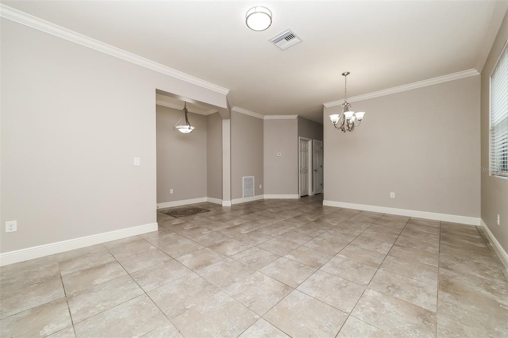An open-concept dining area features light-colored tile flooring, neutral walls, and two hanging chandeliers — 10152 CELTIC ASH DRIVE, RUSKIN, FL