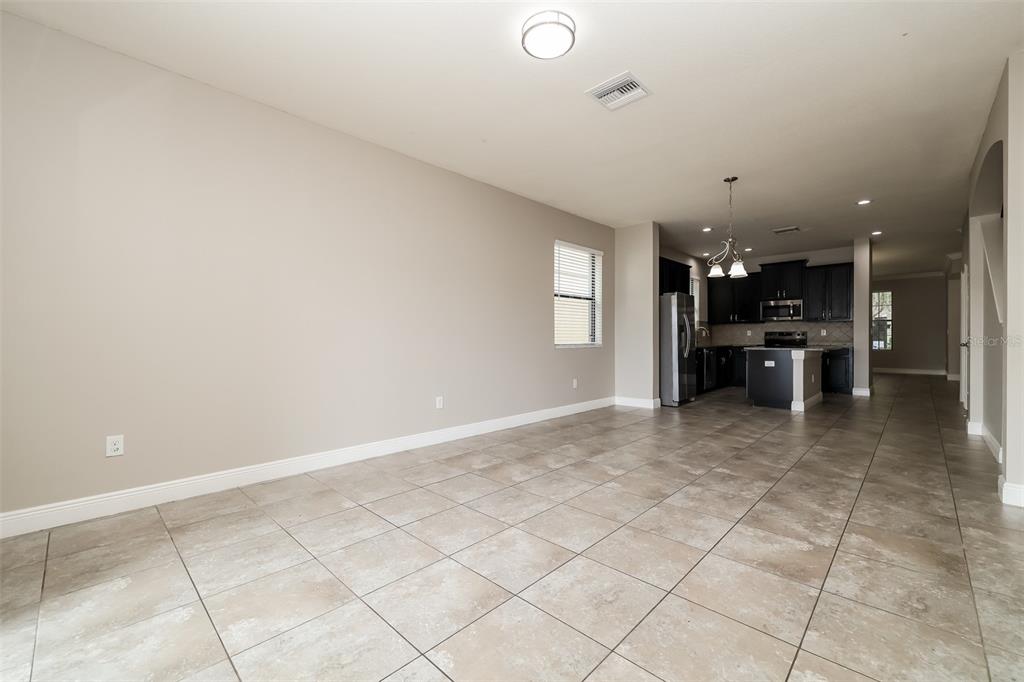 An open-concept living area with tile flooring leads into a kitchen with dark cabinetry — 10152 CELTIC ASH DRIVE, RUSKIN, FL