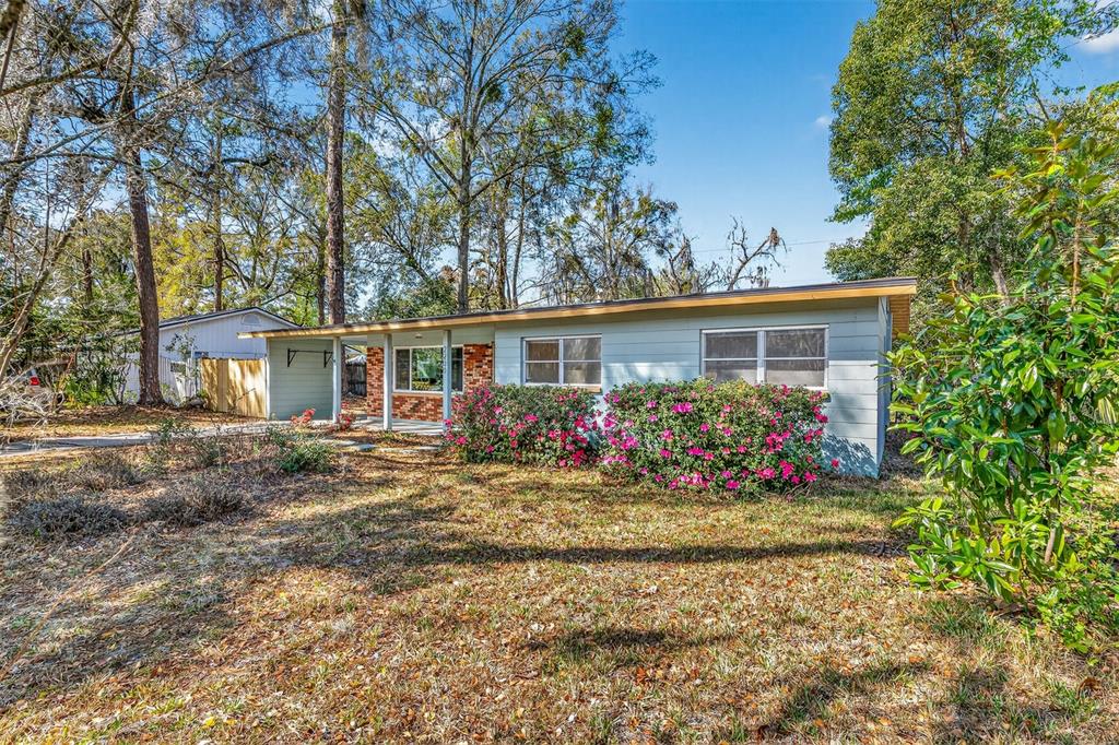 A single-story house with light blue siding, a brick accent wall, and blooming azalea bushes — 2200 NE 16TH TERRACE, GAINESVILLE, FL
